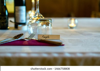 Silverware, napkin, glassware and candles sit on a white tablecloth at a dinner with a place card that reads Family in Italian.