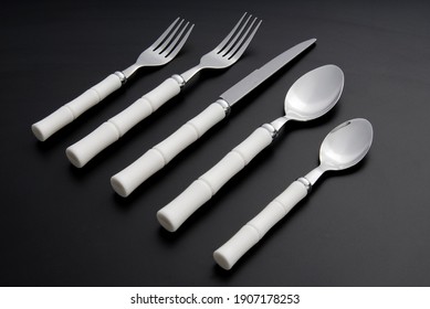 Silverware set isolated on a black background, with painted white bamboo handle.