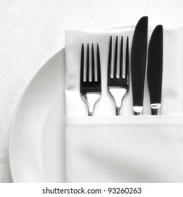 Silverware In White Linen Napkin, On White Plate.