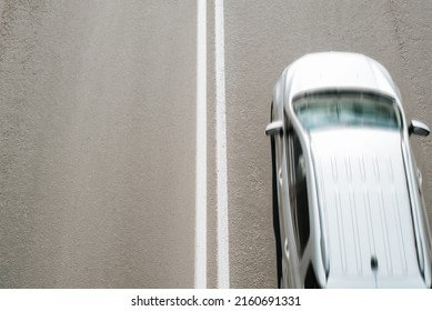 Silvery car driving at fast speed on road, top view. Blurred fast motion, selective focus on dividing double solid marking line on asphalt, copy space.