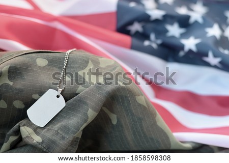 Silvery military beads with dog tag on United States fabric flag and camouflage uniform