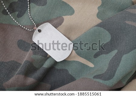 Silvery military beads with dog tag on camouflage fatigue uniform. Army token on soldiers camo jacket rear part