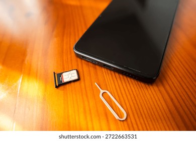 Sim Card and Eject Pin next to smartphone. nano sim card on desk, close-up