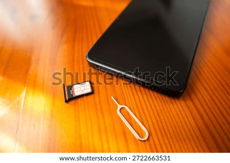 Sim Card and Eject Pin next to smartphone. nano sim card on desk, close-up