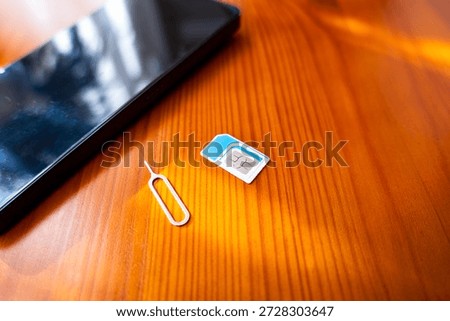 Sim Card and Eject Pin next to smartphone. nano sim card on desk, close-up