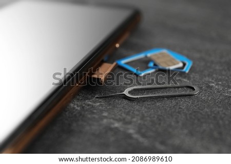 SIM card, mobile phone and ejector tool on grey table, closeup