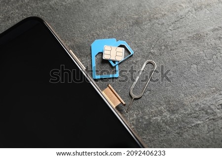 Sim card, mobile phone and ejector tool on grey table, closeup