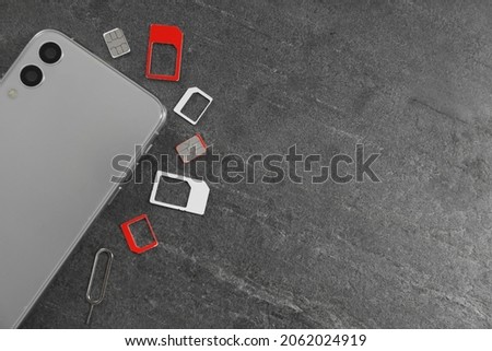 SIM cards, mobile phone and ejector tool on grey table, flat lay. Space for text