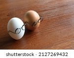 Similar but different concept. White egg and brown egg wear glasses on wooden table