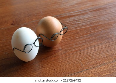 Similar But Different Concept. White Egg And Brown Egg Wear Glasses On Wooden Table