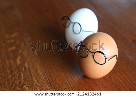 Similar but different concept. White egg and brown egg wear glasses on wooden table