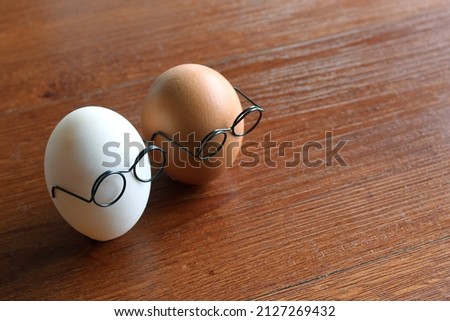 Similar but different concept. White egg and brown egg wear glasses on wooden table