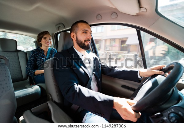 Similing taxi\
driver talking with female passenger.\
