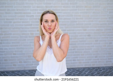 Simpering blond woman holding her hands to her cheeks pursing her lips for the camera - Shutterstock ID 2191656221