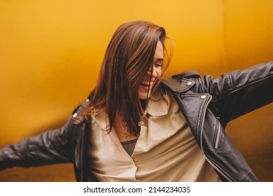 Simpering young brunette woman with a coy smile as she flirts over a gold studio background with copy space. Woman wear black leather jacket and beige shirt is laughing. Focus on hair. - Shutterstock ID 2144234035