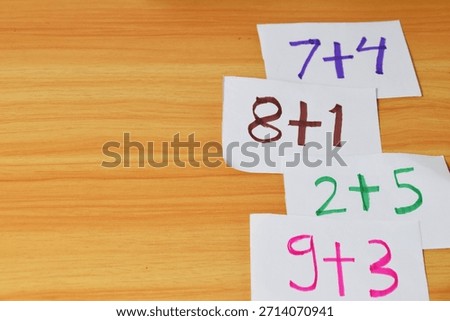 Simple addition math problems written on small white flashcards, stacked on a warm wooden table. Concept for early math education and learning.