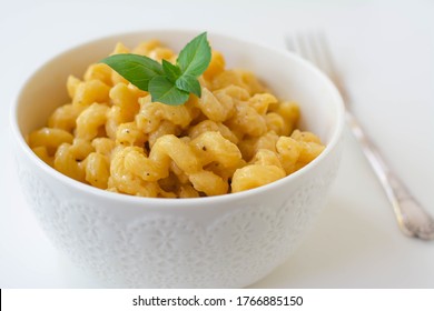 Simple American Stove-top Elbow Macaroni And Cheese Also Called Mac N Cheese Garnished With Basil On White Background