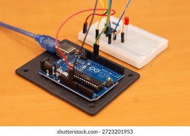 A simple Arduino microcontroller circuit featuring light-emitting diodes (LEDs) connected with resistors on a breadboard, demonstrating a basic alternating signal flasher or dual-channel output indicator for electronics beginners. Comprehensive collection of electronic components featuring an Arduino Uno R3 microcontroller board as the central processing unit for a DIY robotics project. The layout includes a variety of essential hardware for electrical engineering and prototyping, such as a white solderless breadboard, colorful male-to-male jumper wires, light-emitting diodes (LEDs) in various colors, carbon film resistors for current limiting, and integrated circuit sensors. This high-angle shot captures the essence of STEM education, hands-on learning, and the Maker Movement. Perfect for themes involving Internet of Things (IoT) development, computer science curriculum, automated system design, and hardware programming. The arrangement showcases the precision of modern circuitry and the accessibility of open-source hardware for students, engineers, and hobbyists building smart home devices or autonomous robot prototypes.