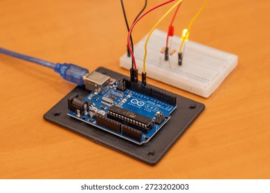 A simple Arduino microcontroller circuit featuring light-emitting diodes (LEDs) connected with resistors on a breadboard, demonstrating a basic alternating signal flasher or dual-channel output indicator for electronics beginners. Comprehensive collection of electronic components featuring an Arduino Uno R3 microcontroller board as the central processing unit for a DIY robotics project. The layout includes a variety of essential hardware for electrical engineering and prototyping, such as a white solderless breadboard, colorful male-to-male jumper wires, light-emitting diodes (LEDs) in various colors, carbon film resistors for current limiting, and integrated circuit sensors. This high-angle shot captures the essence of STEM education, hands-on learning, and the Maker Movement. Perfect for themes involving Internet of Things (IoT) development, computer science curriculum, automated system design, and hardware programming. The arrangement showcases the precision of modern circuitry and the accessibility of open-source hardware for students, engineers, and hobbyists building smart home devices or autonomous robot prototypes.