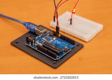 A simple Arduino microcontroller circuit featuring light-emitting diodes (LEDs) connected with resistors on a breadboard, demonstrating a basic alternating signal flasher or dual-channel output indicator for electronics beginners. Comprehensive collection of electronic components featuring an Arduino Uno R3 microcontroller board as the central processing unit for a DIY robotics project. The layout includes a variety of essential hardware for electrical engineering and prototyping, such as a white solderless breadboard, colorful male-to-male jumper wires, light-emitting diodes (LEDs) in various colors, carbon film resistors for current limiting, and integrated circuit sensors. This high-angle shot captures the essence of STEM education, hands-on learning, and the Maker Movement. Perfect for themes involving Internet of Things (IoT) development, computer science curriculum, automated system design, and hardware programming. The arrangement showcases the precision of modern circuitry and the accessibility of open-source hardware for students, engineers, and hobbyists building smart home devices or autonomous robot prototypes.