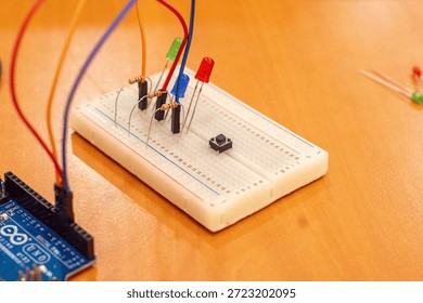 A simple Arduino microcontroller circuit featuring light-emitting diodes (LEDs) connected with resistors on a breadboard, demonstrating a basic alternating signal flasher or dual-channel output indicator for electronics beginners. Comprehensive collection of electronic components featuring an Arduino Uno R3 microcontroller board as the central processing unit for a DIY robotics project. The layout includes a variety of essential hardware for electrical engineering and prototyping, such as a white solderless breadboard, colorful male-to-male jumper wires, light-emitting diodes (LEDs) in various colors, carbon film resistors for current limiting, and integrated circuit sensors. This high-angle shot captures the essence of STEM education, hands-on learning, and the Maker Movement. Perfect for themes involving Internet of Things (IoT) development, computer science curriculum, automated system design, and hardware programming. The arrangement showcases the precision of modern circuitry and the accessibility of open-source hardware for students, engineers, and hobbyists building smart home devices or autonomous robot prototypes.