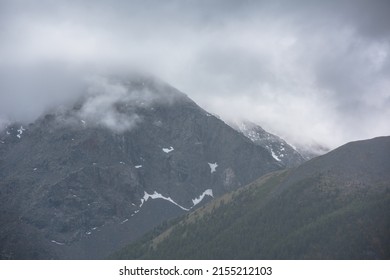 Simple atmospheric rainy landscape with misty forest on mountainside and high mountain among gray low clouds. Bleak overcast scenery with mountain under gray cloudy sky. Gloomy alpine aerial view.
