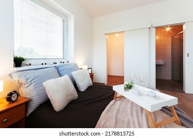 Simple Bedroom In Apartment With Walk-in Closet And Small Bathroom Hidden Behind Sliding Door. In Addition To Bed, There Are Bedside Tables, Lamps, Two Windows And A Tray With Cups On The Bed.