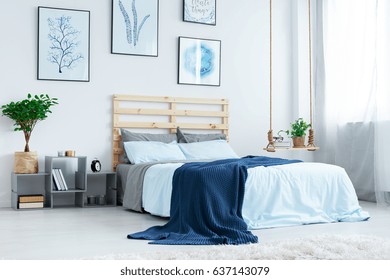 Simple bedroom with double bed, blue bedding, posters and window - Shutterstock ID 637143079