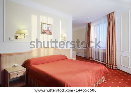 Simple bedroom with double bed with red linen, red carpet and window.