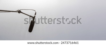 Simple black studio mic, microphone hanging placed on a long high top mic arm stand, plain gray simple background wide copy space, audio voice recording studio, live symbol, abstract concept, nobody