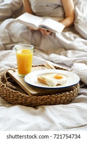 Simple breakfast in bed. Fried eggs with orange juice on tray. Girl with book in the background