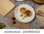 Simple breakfast flat lay with two fresh bread rolls and green grapes on a white plate, set on a rustic grey table with strawberries.