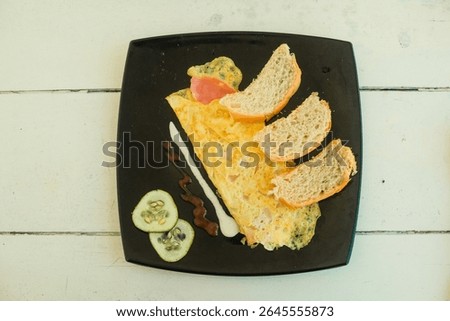 Simple breakfast of omelette, sliced bread, cucumber on black plate on rustic white wooden table. Morning meal in local restaurant, close up top-down view. Travel food photography Varadero, Cuba
