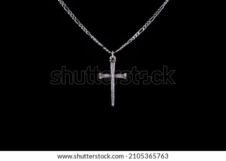 Simple Christian cross and chain necklace isolated on black background with copy space for text. Crucifix hanging on a silver chain