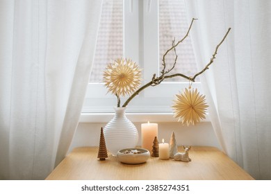 Simple Christmas decoration with two paper stars hanging on bare branches, candles and small natural objects on a table by the window, winter home décor, copy space, selected soft focus - Powered by Shutterstock