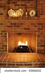 Simple Clean Brick Fireplace With A Single Fire Log Burning Out To Give Heat. There Are Christmas Plates Decorating It At The Top, But Those Can Be Cropped Out To Remove Any Holiday Type Theme.