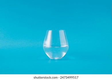 A simple and clean image featuring a half-filled glass of water against a vibrant blue background. The minimalist design highlights the clarity of the water and the glass, creating a refreshing - Powered by Shutterstock