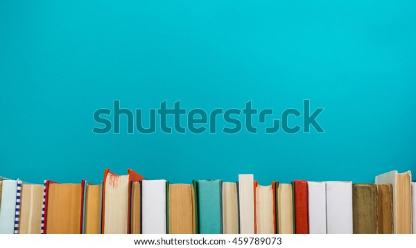 Simple composition of hardback books, raw of books on\
wooden deck table and blue background. Books stacking with no\
labels, blank spine Back to school Copy Space Education background\
Office supplies 