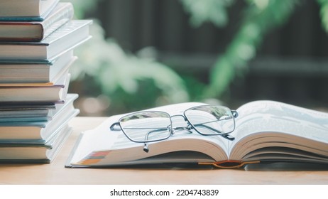 A simple composition of many books, stack or pile of books on wooden table, one of them open and glasses with icons save CO2 and energy sources for renewable concept.