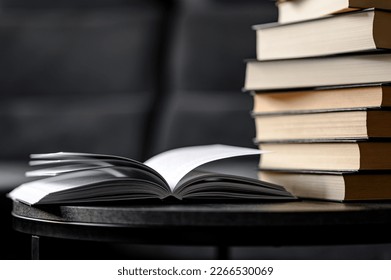 A simple composition of many books, a stack or pile of books on a small table in the living room, one of which is open to finish reading.