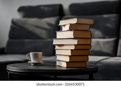 A simple composition of many books, a stack or pile of books on a small table in the living room, next to cup of coffe.