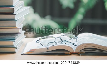 A simple composition of many books, stack or pile of books on wooden table, one of them open and glasses with icons save CO2 and energy sources for renewable concept.