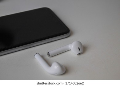 
Simple composition of a mobile phone and wireless headphones on a white surface.