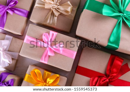 Simple composition with multiple presents wrapped in hand made blank craft paper gift wrap, pastel satin bow. Simple giftbox, wrapping, giftwrap, silk ribbon. Pink background, close up, copy space.