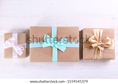 Simple composition with multiple presents wrapped in hand made blank craft paper gift wrap, pastel satin bow. Simple giftbox, wrapping, giftwrap, silk ribbon. Pink background, close up, copy space.