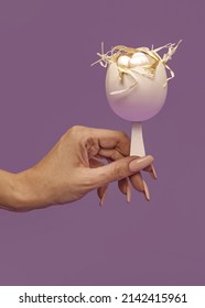 A Simple Concept Of Easter. Half Of A White Egg Shell Decorated With Light Hay. A Female Hand Holds A White Egg On A Ice Cream Stick . The Hipster Idea Of A Modern Easter. Pastel Background.