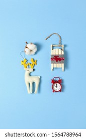 Simple creative Christmas composition. Cotton box, deer, wooden sled, alarm clock on blue background, copy space. Minimal style. Top view. Vertical. For social media, greeting card, office supplies.