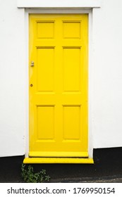 Simple design wooden yellow front door to a residential home property The surrounding wall is white with a black base.