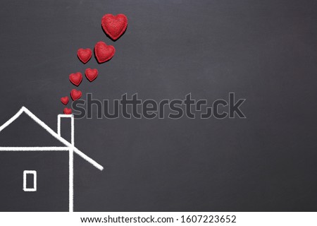 simple drawing house with white chalk on a black board, red textural hearts in the form of smoke from a chimney, the concept of a friendly happy family, living together under one roof, love in home