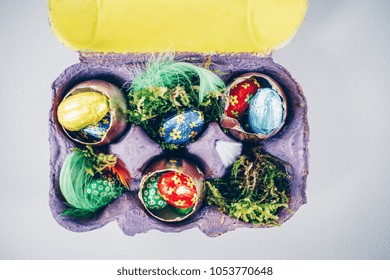 Simple Easter Decoration With Chocolate Eggs , Golden Painted Egg Shells And Natural Materials In Egg Carton Painted Violet And Yellow. View From Above, Copy Space.